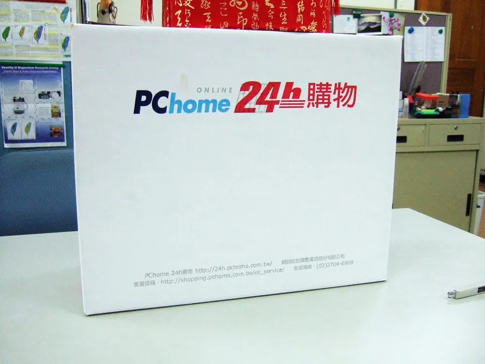A white shipping box printed with the PChome ONLINE 24h shopping logo and website addresses sits on a white desk in an office.