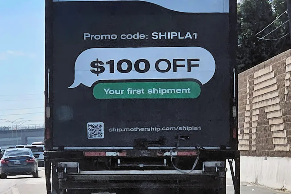 Rear of a black delivery truck on a highway showing a Mothership.com promo banner offering $100 off a first shipment.