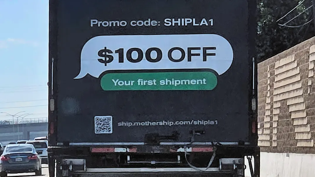 Rear of a black delivery truck on a highway showing a Mothership.com promo banner offering $100 off a first shipment.