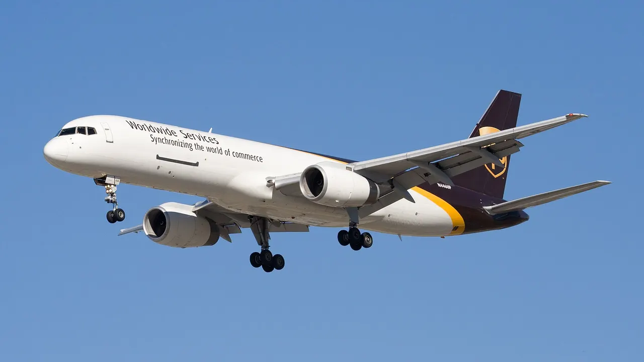 A white cargo jet with purple and gold tail livery and the text 'Worldwide Services' on its fuselage flies against a clear blue sky with landing gear extended.