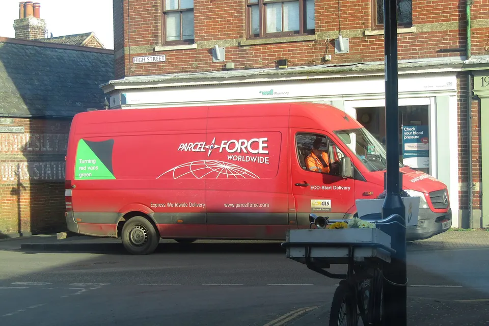 A red Parcelforce Worldwide van marked ECO-Start Delivery is parked beside a brick building on a street with a High Street sign.